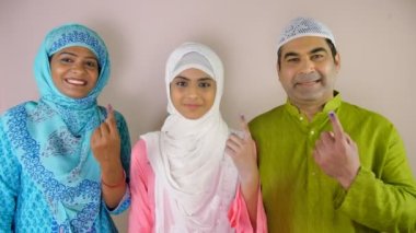 Şirin bir Müslüman kız ve ailesi dövmeli parmaklarını göstermekten mutlu olurlar. Hint vatandaşı, kimlik damgası, devlet seçimleri. Genç bir Hintli aile oylarını verdikten sonra kameraya poz verirken bir arada duruyor - temel haklar, ...