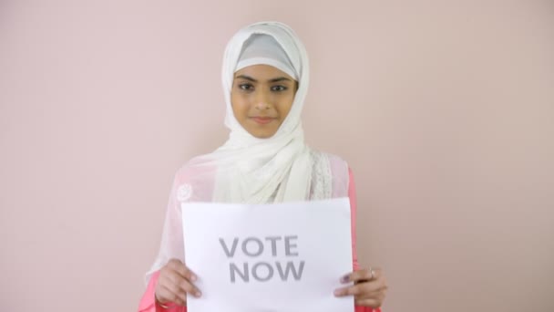 一个戴着白色头巾的漂亮女孩拿着一张纸 上面写着 现在就投票 州选举 竞选活动 负责任的公民 一名年轻的穆斯林少女 穿着头巾 投票后高兴地在镜头前摆姿势 印度花旗 — 图库视频影像