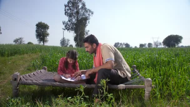 彼女の宿題で彼の娘を助ける教育を受けたインドの村人 女の子の子供の教育 Beti Bachao Beti Padhao 編組髪の若い女の子と彼女の父親 インドの農業 インドの村のホームシーン — ストック動画