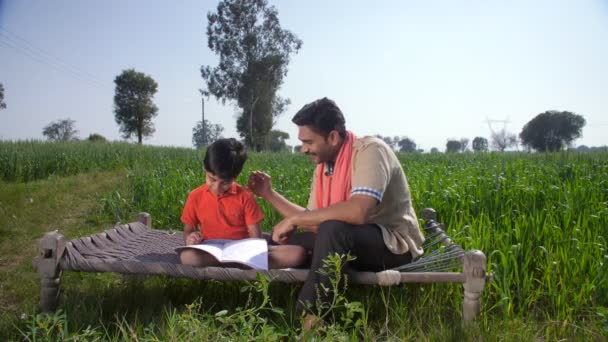 一位英俊的留胡子农民正在帮助他的小儿子完成他的家庭作业 学校作业 乡村教育 一个可爱的男孩 来自一个印第安村庄 和他的父亲一起学习 同时坐在他的农田里 亲子关系 — 图库视频影像