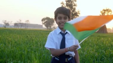 Hindistan Ulusal Bayrağı 'nı sallayan okul üniformalı genç bir çocuk - Bağımsızlık / Cumhuriyet Günü. Kızılderili köyünden neşeli küçük bir çocuk tarım tarlasında dururken elinde Hint bayrağı tutuyordu.