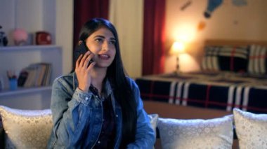 Oturma odasında cep telefonunu kullanarak telefon eden genç bir üniversite öğrencisi. Boş zaman. Uzun saçlı, rahat bir kanepede dinlenen güzel bir kadın. Rahat bir oda, kış mevsimi.