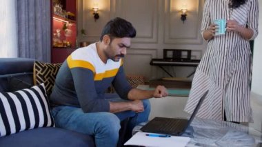 Orta yaşlı, stresli bir işadamı, ofisini dizüstü bilgisayarıyla yapıyor. Evden çalışıyor, Covid yaşam tarzı, internet bağlantısı. Şefkatli bir Hintli ev kadını kocasına bir fincan sıcak çay ve kahve veriyor. Bir içecek, sevgi dolu bir aile.