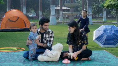 Genç, neşeli bir çift sevimli sevimli oğluyla güzel vakit geçiriyor. Mutlu ebeveynlik, ilişki ve birliktelik. Küçük tatlı bir kız, parkta arkasını yaslayıp annesine sarılıyor. Sevgi ve şefkat dolu, mutlu bir çocukluk.