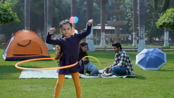 一个年轻的印度小女孩在玩呼啦圈 一项户外运动 一项儿时的游戏 一个印度家庭 一个公园里的家庭野餐 一位印度的丈夫和妻子在公园里陪着孩子 快乐地养育孩子 — 图库视频影像