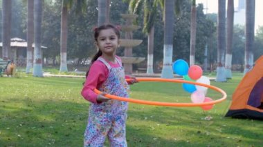 Günlük kıyafetlerle dans eden, hula-hoop ile pratik yapan küçük tatlı bir kız. Açık hava egzersizi, eğlenceli aktivite. Şehir parkında Hula-basket oyuncağıyla oynayan sevimli bir kız çocuğu - boş zaman, eğlence ve eğlence, yaşam tarzı ve fitness