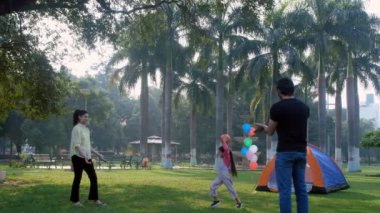 Aile pikniği - genç Hintli ebeveynler kızlarıyla oynuyorlar, anne-kız kaynaşması, eğlenceli bir oyun. Neşeli bir Hintli aile dışarıda eğleniyor. Halk parkı, boş zaman, aile bağı, nükleer bir aile.