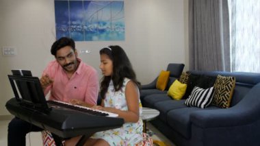 Orta yaşlı bir müzik öğretmeni Hintli bir kızı klavye / piyano ile eğitiyor. Müzik aleti, baba-kız kaynaşması. Hintli bir baba ve küçük kızı oturma odasında eğlenceli bir aktivite yapıyorlar. Boş zaman, mutlu bir çocukluk.