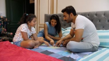 Evli bir Hintli çift ve küçük kızları birlikte uçan kuş oyunu oynuyorlar, Chidiya Udd, çocukluk oyunu. Modern neşeli bir aile yatak odasında birlikte kaliteli zaman geçirir. Eğlenceli bir aktivite, boş zaman, aile bağı.