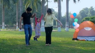 Parkta kızlarıyla oynayan mutlu bir Hintli çift. Akrobasi, jimnastik. Modern bir çekirdek aile ve onların küçük çocukları piknik zamanı, boş zaman, yeni nesil ebeveynlik, birliktelik ve ilişki.