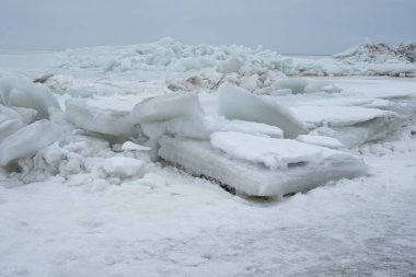 Donmuş deniz. Kıyıda yığılmış kocaman buz kalıpları. Kumsalda fırtınalı hava.