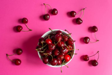 Pembe arka planda beyaz bir kasede kırmızı kirazlar