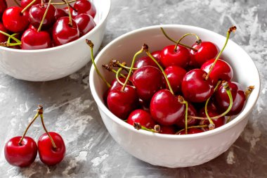 Gri taşlı arka planda beyaz bir kasede kırmızı kirazlar