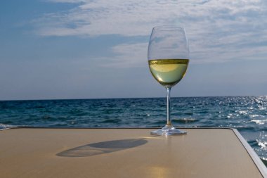Bir bardak beyaz şarap. Deniz kıyısının arka planında şarap ve güneşli bir yaz plajı. Tatil köyünde şarap tatma ve rahatlama.