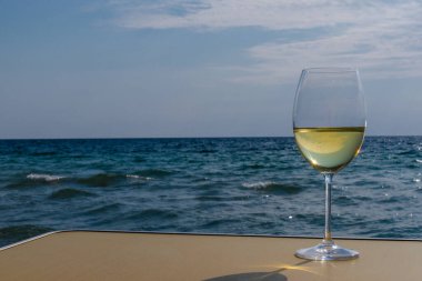 Bir bardak beyaz şarap. Deniz kıyısının arka planında şarap ve güneşli bir yaz plajı. Tatil köyünde şarap tatma ve rahatlama.
