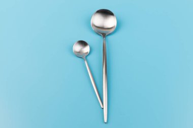 Temiz, boş bir masa kaşığı ve mavi arka planda küçük kaşıklar. Yemek ve mutfak eşyaları konsepti