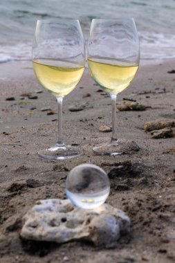 Bir bardak beyaz şarap. Deniz kıyısının arka planında şarap ve güneşli bir yaz plajı. Tatil köyünde şarap tatma ve rahatlama.