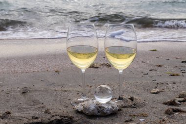 Bir bardak beyaz şarap. Deniz kıyısının arka planında şarap ve güneşli bir yaz plajı. Tatil köyünde şarap tatma ve rahatlama.