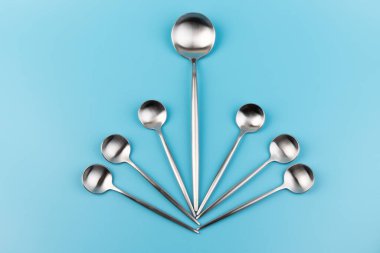 Temiz, boş bir masa kaşığı ve mavi arka planda küçük kaşıklar. Yemek ve mutfak eşyaları konsepti