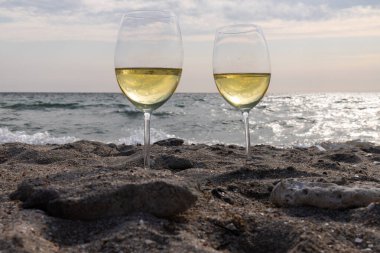 Bir bardak beyaz şarap. Deniz kıyısının arka planında şarap ve güneşli bir yaz plajı. Tatil köyünde şarap tatma ve rahatlama.
