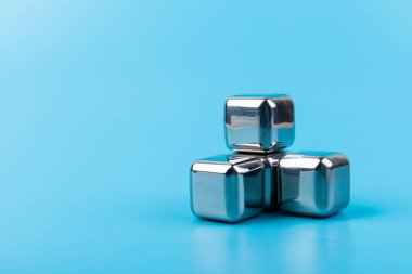 Mavi arka planda izole edilmiş paslanmaz çelik buz küpleri viski taşları. Metin için boşluk.