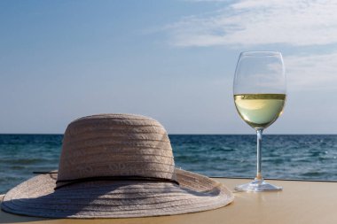 Bir bardak beyaz şarap. Deniz kıyısının arka planında şarap ve güneşli bir yaz plajı. Tatil köyünde şarap tatma ve rahatlama.