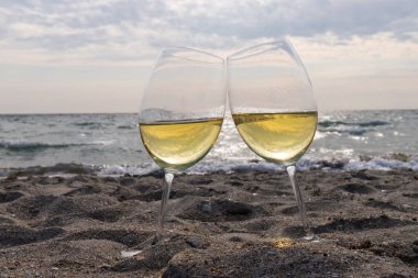 Bir bardak beyaz şarap. Deniz kıyısının arka planında şarap ve güneşli bir yaz plajı. Tatil köyünde şarap tatma ve rahatlama.