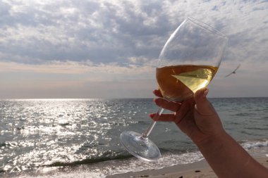 Bir bardak beyaz şarap. Deniz kıyısının arka planında şarap ve güneşli bir yaz plajı. Tatil köyünde şarap tatma ve rahatlama.