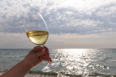 Bir bardak beyaz şarap. Deniz kıyısının arka planında şarap ve güneşli bir yaz plajı. Tatil köyünde şarap tatma ve rahatlama.