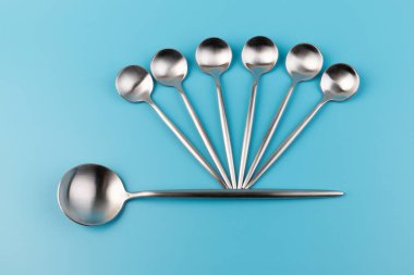 Temiz, boş bir masa kaşığı ve mavi arka planda küçük kaşıklar. Yemek ve mutfak eşyaları konsepti