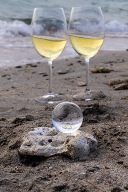 Bir bardak beyaz şarap. Deniz kıyısının arka planında şarap ve güneşli bir yaz plajı. Tatil köyünde şarap tatma ve rahatlama.