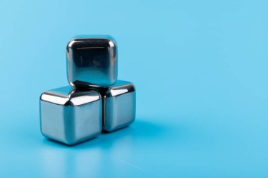 Mavi arka planda izole edilmiş paslanmaz çelik buz küpleri viski taşları. Metin için boşluk.