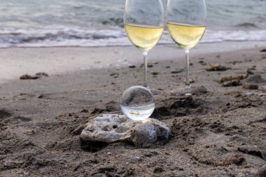 Bir bardak beyaz şarap. Deniz kıyısının arka planında şarap ve güneşli bir yaz plajı. Tatil köyünde şarap tatma ve rahatlama.