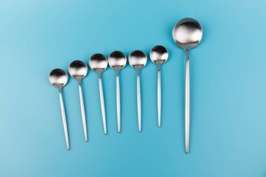 Temiz, boş bir masa kaşığı ve mavi arka planda küçük kaşıklar. Yemek ve mutfak eşyaları konsepti