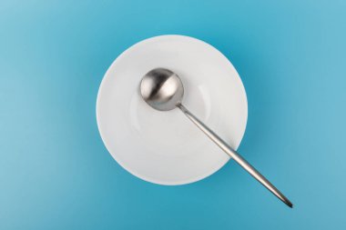 Mavi arka planda kaşığı olan boş bir tabak. Üst Manzara. Mutfak Utensil.