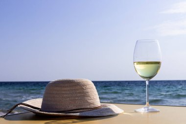 Bir bardak beyaz şarap. Deniz kıyısının arka planında şarap ve güneşli bir yaz plajı. Tatil köyünde şarap tatma ve rahatlama.