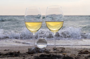 Bir bardak beyaz şarap. Deniz kıyısının arka planında şarap ve güneşli bir yaz plajı. Tatil köyünde şarap tatma ve rahatlama.