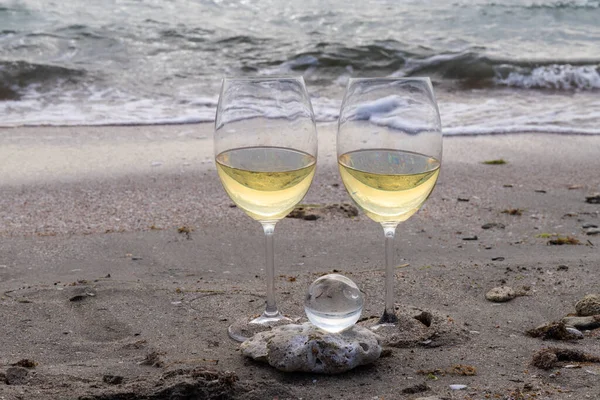 Bir bardak beyaz şarap. Deniz kıyısının arka planında şarap ve güneşli bir yaz plajı. Tatil köyünde şarap tatma ve rahatlama.