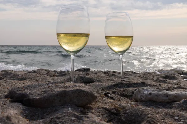 Bir bardak beyaz şarap. Deniz kıyısının arka planında şarap ve güneşli bir yaz plajı. Tatil köyünde şarap tatma ve rahatlama.