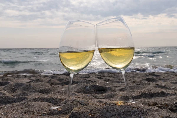 Bir bardak beyaz şarap. Deniz kıyısının arka planında şarap ve güneşli bir yaz plajı. Tatil köyünde şarap tatma ve rahatlama.