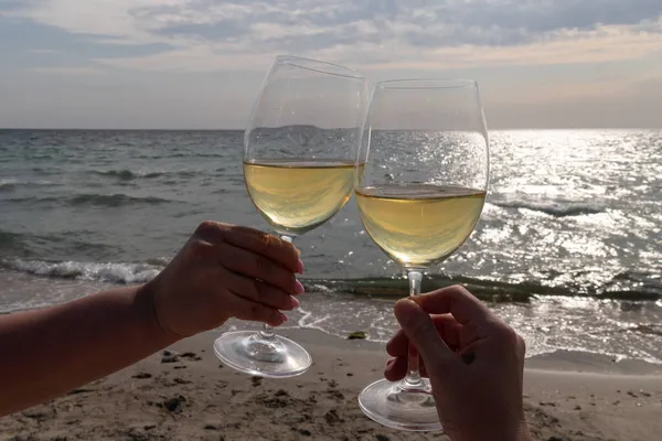 Bir bardak beyaz şarap. Deniz kıyısının arka planında şarap ve güneşli bir yaz plajı. Tatil köyünde şarap tatma ve rahatlama.