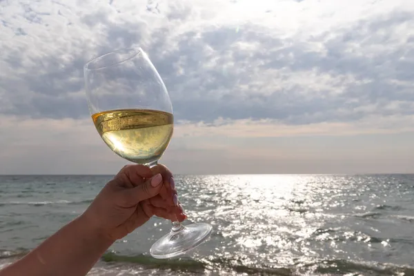 Bir bardak beyaz şarap. Deniz kıyısının arka planında şarap ve güneşli bir yaz plajı. Tatil köyünde şarap tatma ve rahatlama.