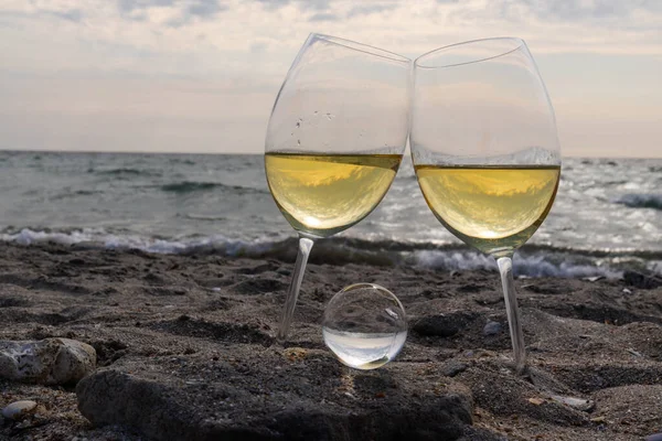 Bir bardak beyaz şarap. Deniz kıyısının arka planında şarap ve güneşli bir yaz plajı. Tatil köyünde şarap tatma ve rahatlama.