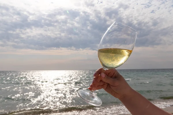 Bir bardak beyaz şarap. Deniz kıyısının arka planında şarap ve güneşli bir yaz plajı. Tatil köyünde şarap tatma ve rahatlama.