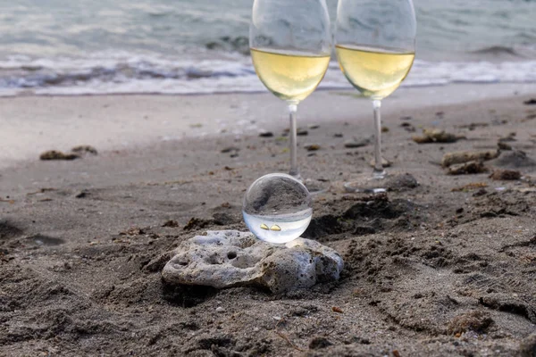 Bir bardak beyaz şarap. Deniz kıyısının arka planında şarap ve güneşli bir yaz plajı. Tatil köyünde şarap tatma ve rahatlama.
