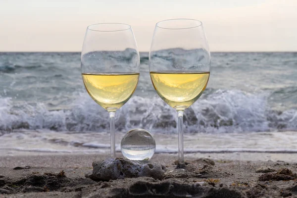 Bir bardak beyaz şarap. Deniz kıyısının arka planında şarap ve güneşli bir yaz plajı. Tatil köyünde şarap tatma ve rahatlama.