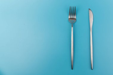 Mavi arka planda çatal ve bıçak. Kahvaltıda, öğle yemeğinde ya da akşam yemeğinde tabaklar düzdü. Üst Manzara. Mutfak Utensil.