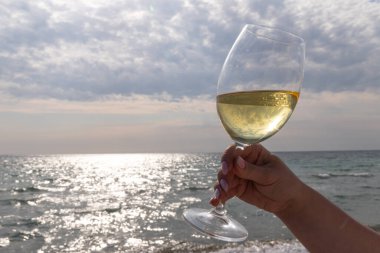 Bir bardak beyaz şarap. Deniz kıyısının arka planında şarap ve güneşli bir yaz plajı. Tatil köyünde şarap tatma ve rahatlama.