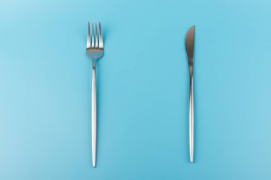 Mavi arka planda çatal ve bıçak. Kahvaltıda, öğle yemeğinde ya da akşam yemeğinde tabaklar düzdü. Üst Manzara. Mutfak Utensil.