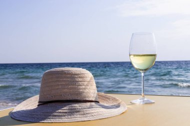 Bir bardak beyaz şarap. Deniz kıyısının arka planında şarap ve güneşli bir yaz plajı. Tatil köyünde şarap tatma ve rahatlama.